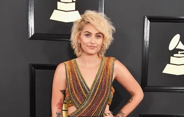 "Person in a shimmering striped dress on a red carpet with Grammy symbols in the background."