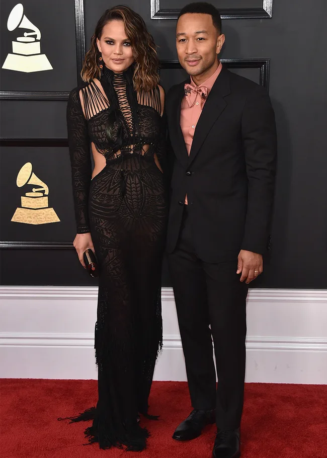 A couple poses on the red carpet at a formal event, with a Grammy logo in the background.
