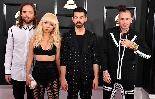 Four individuals in stylish outfits on the red carpet at a music awards event.