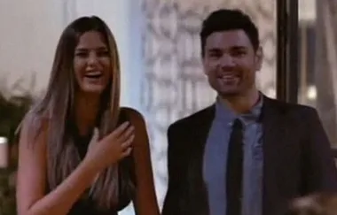 A woman and man dressed formally, smiling and standing indoors, possibly at an event.