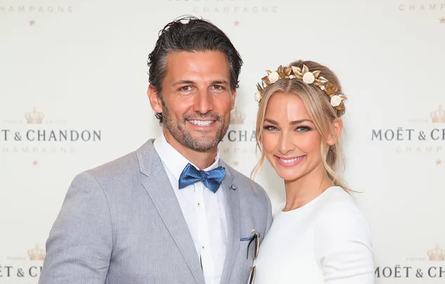 A couple smiling at a Moët & Chandon event; the man in a suit and bow tie, the woman wearing a floral headband.