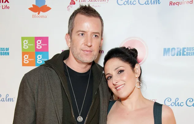 A man and a woman posing together at an event with logo backgrounds.