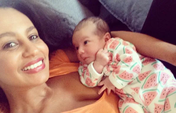 Mother smiling while holding her baby wearing a watermelon-patterned onesie.