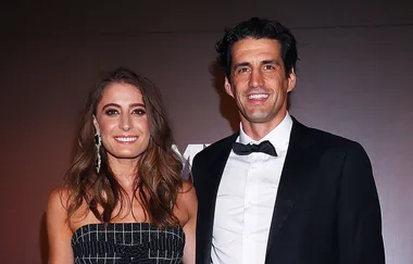 A woman in a strapless dress and a man in a tuxedo smile together on a red carpet.