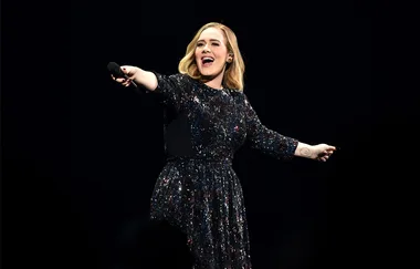 Singer performing on stage in a sparkling dress, holding a microphone and smiling.
