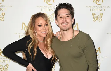 Two smiling individuals pose together in front of a "Mariah Carey I Don't" promotional backdrop.
