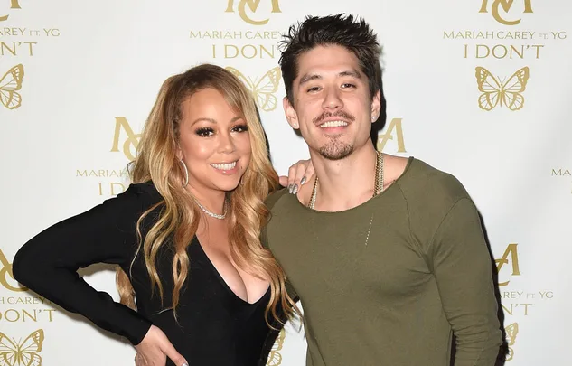 Two smiling individuals pose together in front of a "Mariah Carey I Don't" promotional backdrop.