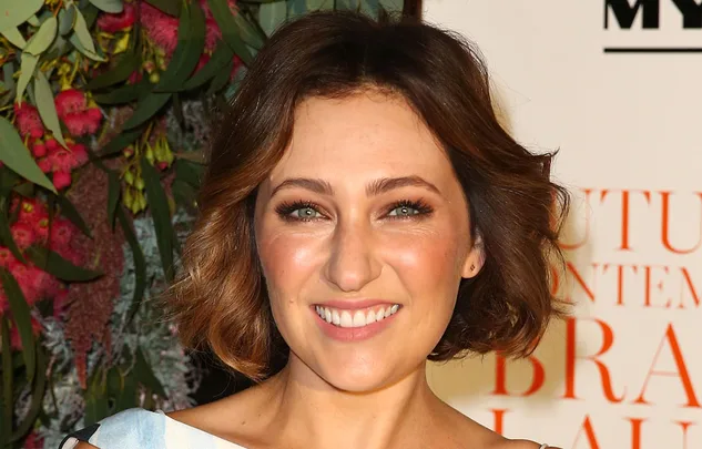 ```html
A woman with short brown hair smiling in front of a flower backdrop.
```