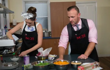 Two contestants wearing "MKR" aprons cooking in a kitchen with bowls and ingredients on the counter.