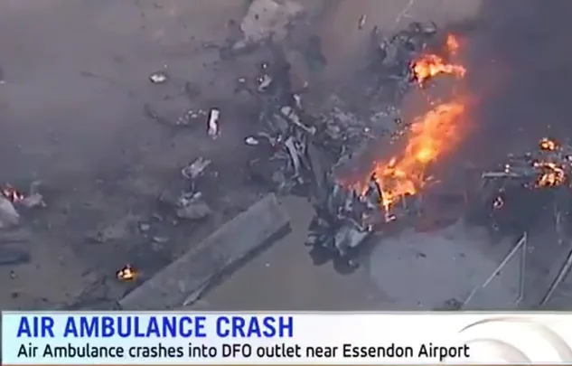 Aerial view of an air ambulance crash with debris and flames near Essendon Airport, as reported on television.