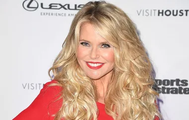 A woman with long blonde hair and a red dress smiles at a Sports Illustrated event.