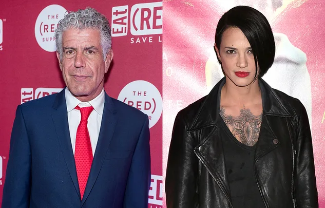 Two individuals at an event, one in a blue suit and red tie, the other in a black leather jacket with a tattoo.