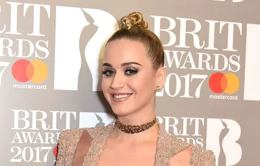 Person smiling at the 2017 Brit Awards, wearing a sparkly choker and topknot hairstyle, with event backdrop.