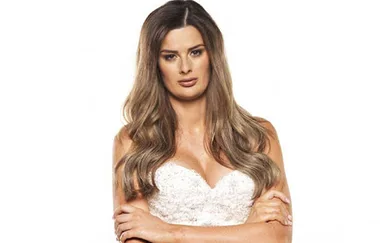 A woman with long hair in a white strapless dress crosses her arms, looking forward.