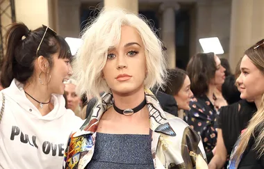 A person with short blonde hair and a colorful jacket stands in a crowded room.