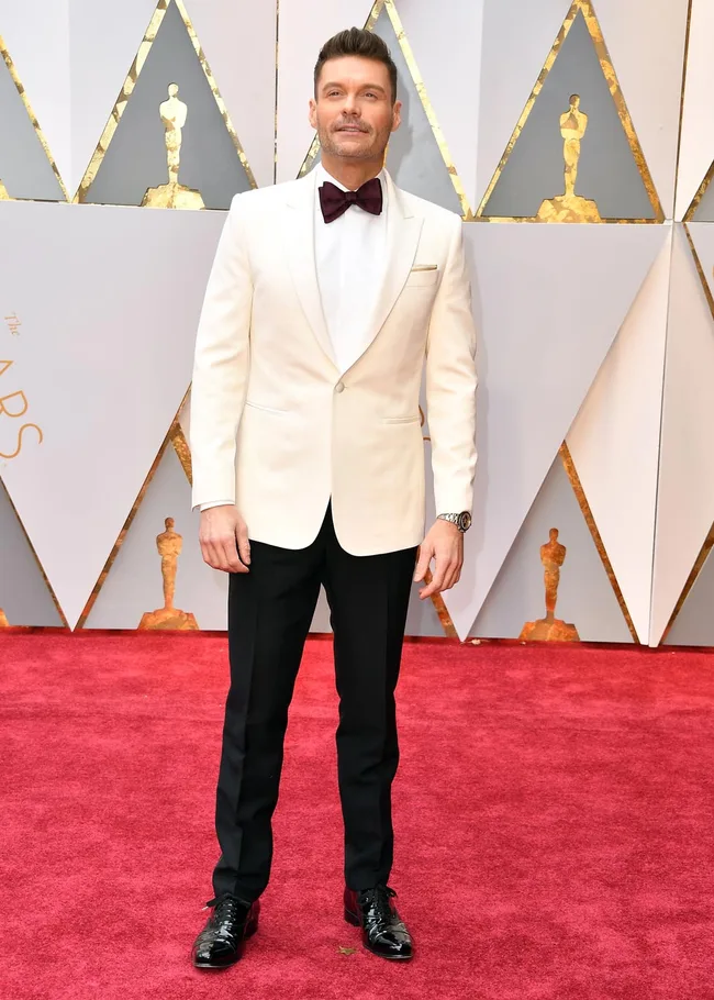 Male celebrity in white tuxedo and bow tie on red carpet at awards event.
