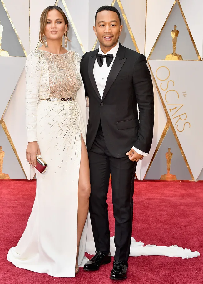 Couple on the Oscars red carpet, woman in an elegant white gown and man in a black tuxedo, posing together.