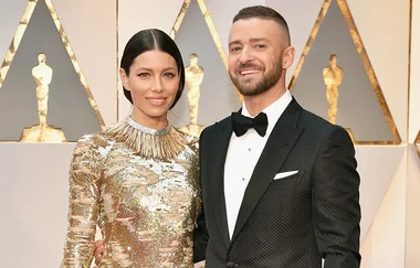 Couple posing on red carpet in formal attire; woman in gold dress, man in black tuxedo.