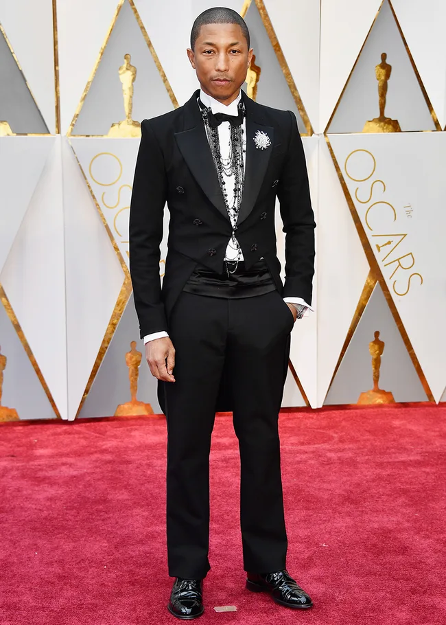 Man in a black tuxedo with ornate jewelry on the red carpet at the Oscars.