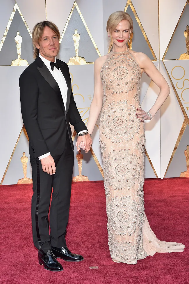 A couple holding hands on the Oscars red carpet.