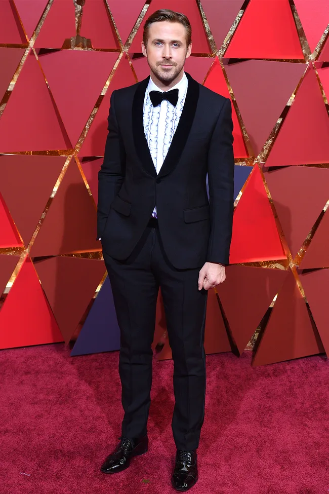 Man in a tuxedo on a red carpet with geometric red background.