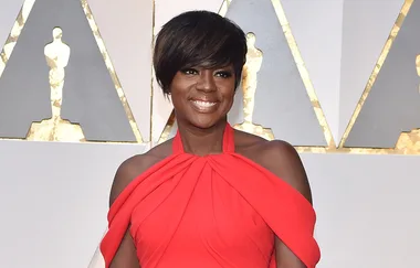Viola Davis in a striking red gown at the Oscars, smiling against a backdrop of the award stage design.
