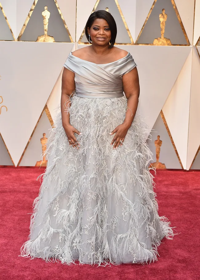 Woman in elegant silver feathered gown on red carpet at awards event.