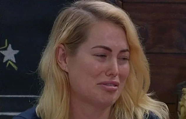 A woman with blonde hair appears upset, with tearful eyes and a pained expression, sitting indoors.