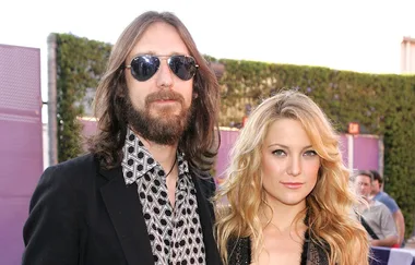 A man in sunglasses and a woman with long blonde hair pose outdoors at an event.