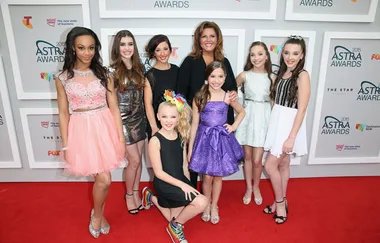 Group of eight people, including young dancers, posing on the red carpet at the 2015 ASTRA Awards.