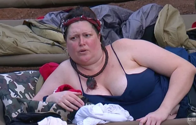 Person in a blue swimsuit, lying on camping gear, appears puzzled or engaged in conversation outdoors.