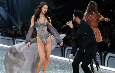 Model in lingerie walks runway, singer performs next to her at a fashion show.