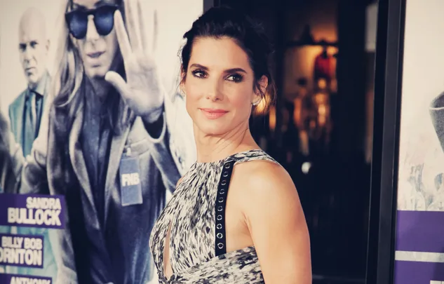 A woman in a patterned dress poses at an event, with a movie poster in the background.