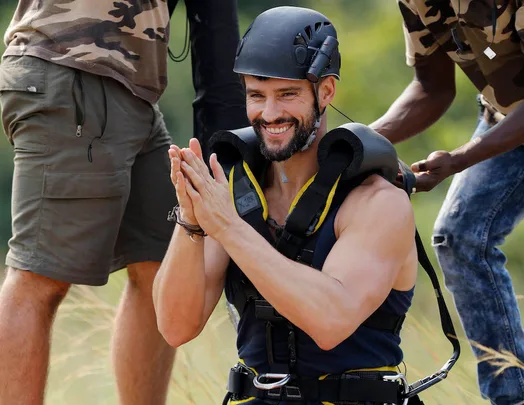 Man smiling while wearing a helmet and harness, flanked by two others, during an outdoor activity.