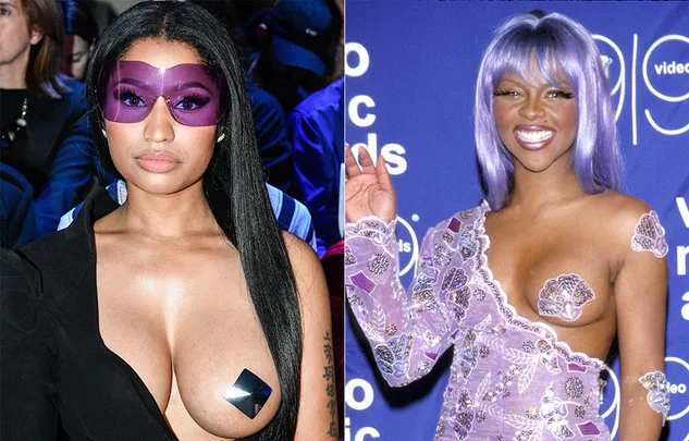 Two women at an event, one wearing large purple glasses, the other with purple hair and a lavender outfit with star pasties.
