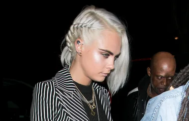 A person with braided silver hair wearing a striped blazer and layered necklaces at a nighttime event.