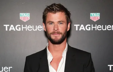 Man in suit at TAG Heuer event, posing in front of branded logo wall.