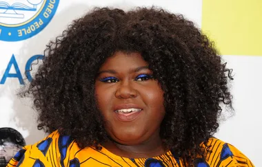 ```html
<img src="url" alt="Person with curly hair and bright makeup at a formal event." />
```