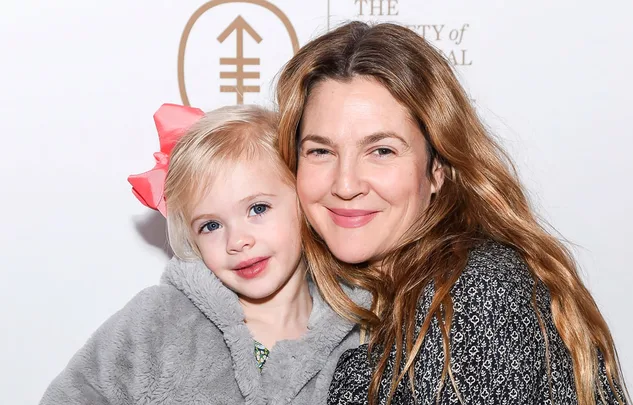 Two smiling people pose together; a child in a gray jacket with a pink bow and an adult with long brown hair.