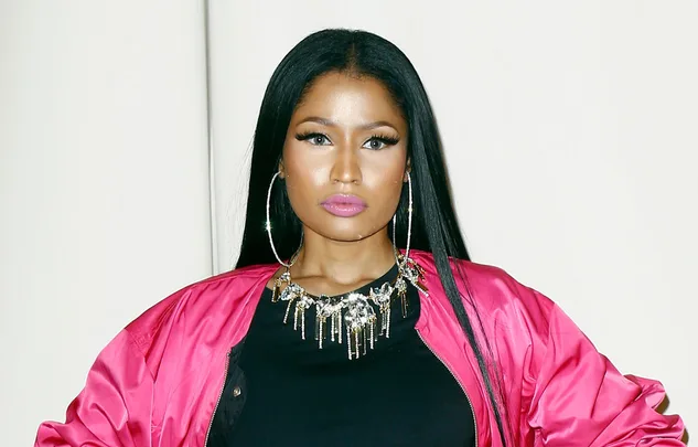 A person wearing a pink jacket, with long black hair and large hoop earrings, posing with a neutral expression.