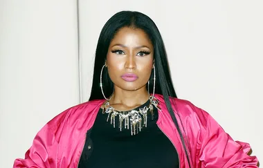 A person wearing a pink jacket, with long black hair and large hoop earrings, posing with a neutral expression.