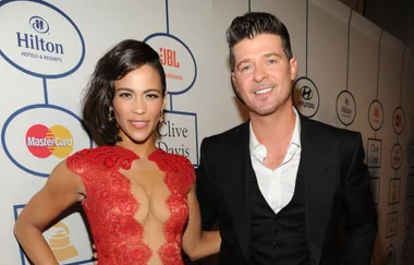 A woman in a red lace dress poses with a man in a black suit at an event with logos on the background wall.