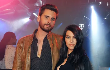 Two people posing together in a dimly lit nightclub setting with colored lights.