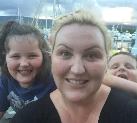 A woman and two children smiling with a marina and boats in the background.