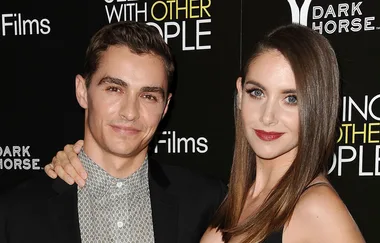 Two people posing on the red carpet at a film event, with a backdrop featuring text and logos.