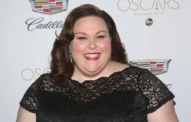 A woman in a black lace dress smiles at an event backdrop featuring Cadillac and Oscars logos.