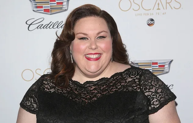 A woman in a black lace dress smiles at an event backdrop featuring Cadillac and Oscars logos.