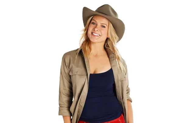 Woman in a cowboy hat smiling, wearing a tan jacket and black top against a white background.