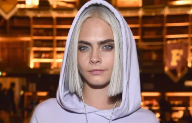 Woman with short blonde hair wearing a hooded sweatshirt, standing indoors with a blurred background.
