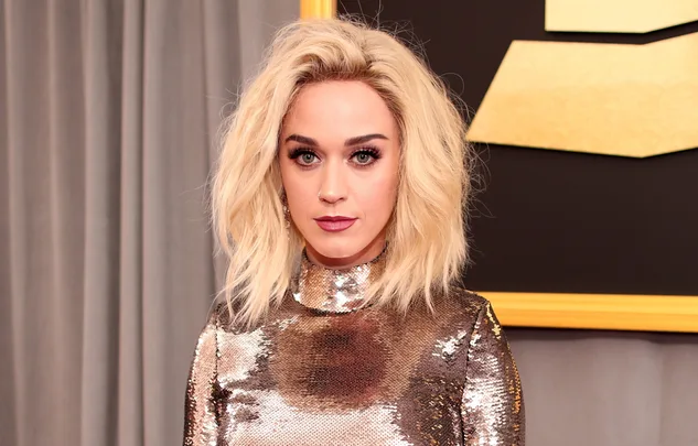 Woman with blonde hair in a sequined dress standing in front of a gray curtain.